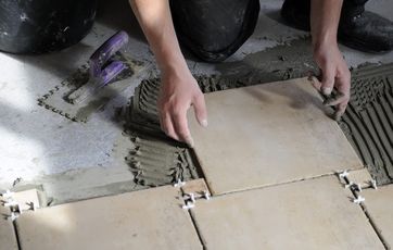 Kvadratiske fliser lægges på et betongulv i badeværelse