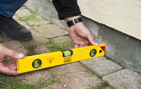 Mand måler fald fra hus med vaterpas