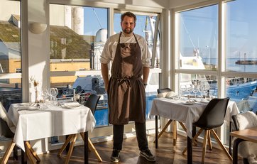 Daniel Kruse i Restaurant Molen foran glasparti med stor fiskekutter lige bagved