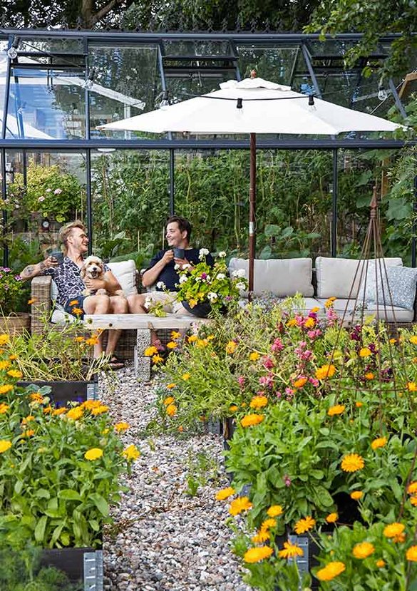 Loungeområde med sofa ved siden af højbede og drivhus