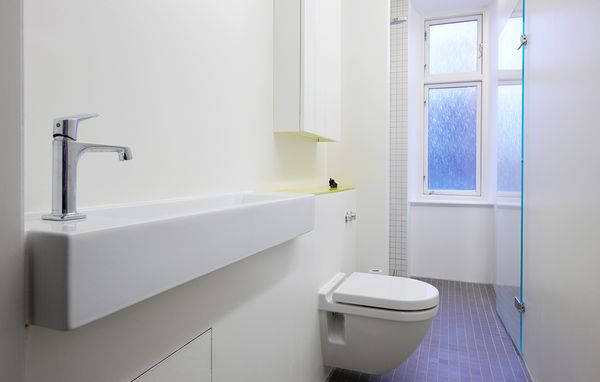 Smalt badeværelse med installationsvæg, smal håndvask og indbygget cisterne