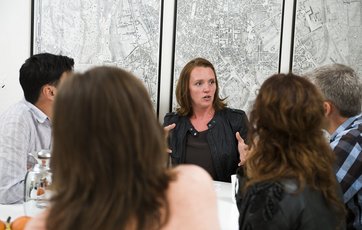 Fem mennesker holder byggemøde ved et hvidt spisebord. Fem mennesker holder byggemøde ved et hvidt spisebord.