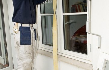 Håndværker står på trappestige og isolerer et vindue