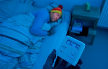 Mand ligger og sover med hue på, mens termometret viser en temperatur på 8,2 grader