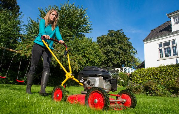 Kvinde slår højt græs med plæneklipper