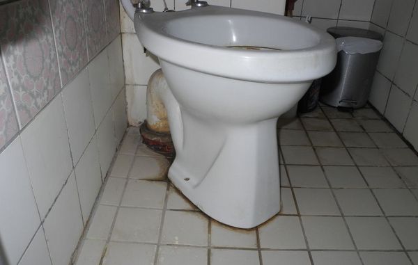 Misfarvede fuger på toilettet. Badeværelse med grå fliser og meget misfarvede fuger.