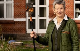 Abelone Glahn står med en rive foran huset