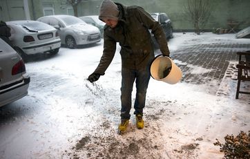 Boligejer spreder grus på fortov.