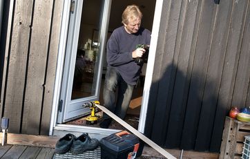 Håndværker sætter ny havedør i et sort sommerhus.