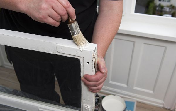 Mand maler vinduesbeslag med hvid maling Mand maler vinduesbeslag med hvid maling