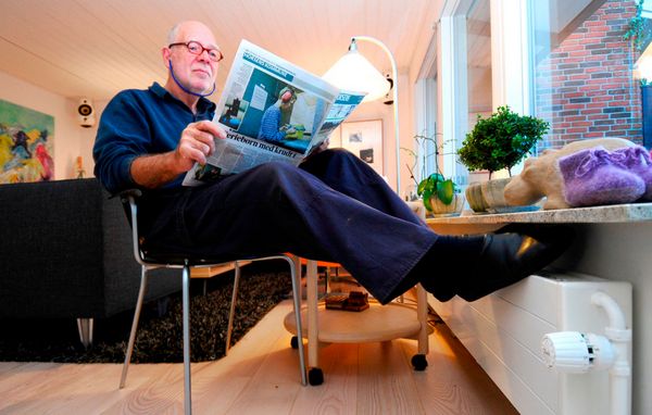 Ældre mand sidder med fødderne på en radiator Ældre mand sidder med fødderne på en radiator