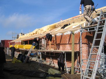 Håndværkere i gang med at mure et hus op med røde mursten. Håndværkere i gang med at mure et hus op med røde mursten.