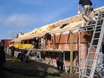 Håndværkere i gang med at mure et hus op med røde mursten. Håndværkere i gang med at mure et hus op med røde mursten.