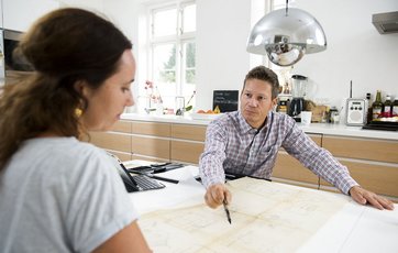 Kvinde og mand ser på konstruktionstegninger ved et bord. Kvinde og mand ser på konstruktionstegninger ved et bord.