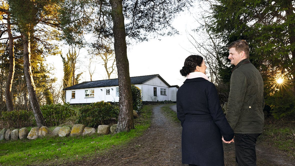 Mand og kvinde står på vej og ser på hinanden med hus i baggrunden