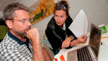 Et par sidder foran pc og med papir i hånden og diskuterer deres boligøkonomi