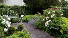 Have med flisesti, terrasse og blomstrende buske