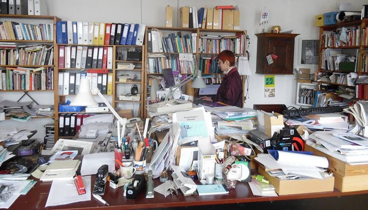 Kvinde arbejder ved skrivebord med store bunker papir