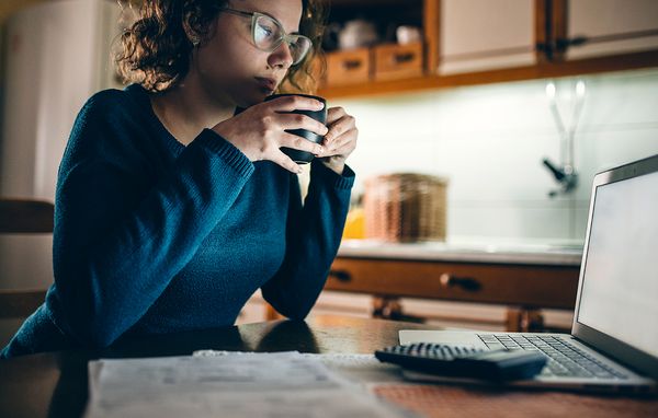 Kvinde sidder og kigger på sin computer med en lommeregner ved siden af