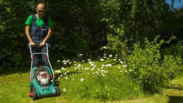 Mand slår græs og plejer sin græsplæne