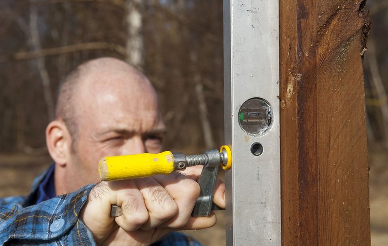 Mand tjekker, om stolpe står lige med vaterpas