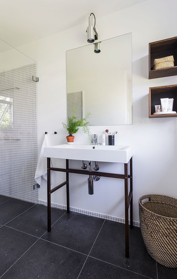 Fliseinspiration8 Små, hvide mosaikfliser i brusenichen og store, sorte fliser på gulvet i et badeværelse.