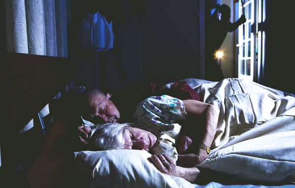 Ældre par sover i soveværelse, mens tyv lyser ind på dem med lommelygte