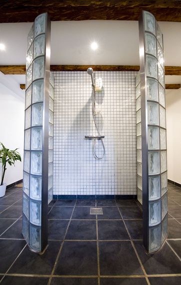 Stor brusekabine med mosaikfliser på væggen og afskærmning udført i glasfliser