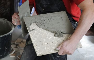 Flisemurer påfører fliselim til bagsiden af en kvadratisk flise