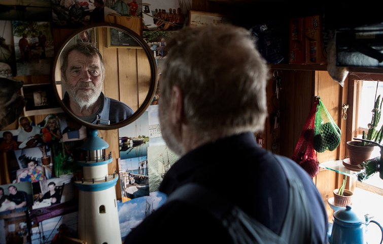 Gert Sømand ser sig selv i spejlet, der hænger blandt masser af billeder