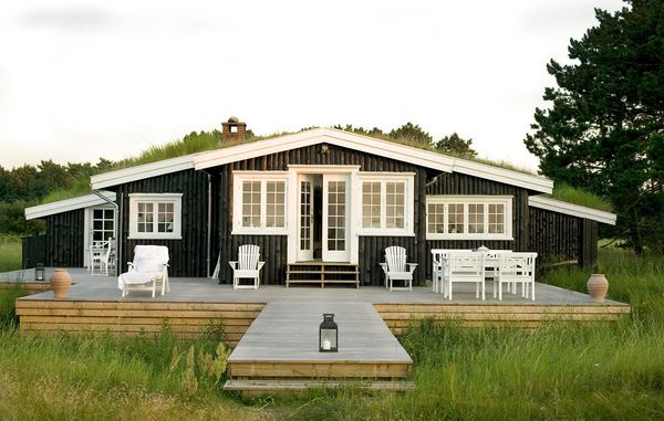 Sommerhus i sortmalet træ med hvide vinduer.
