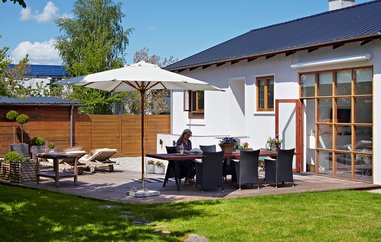 Anne Marie sidder i haven foran sit hus