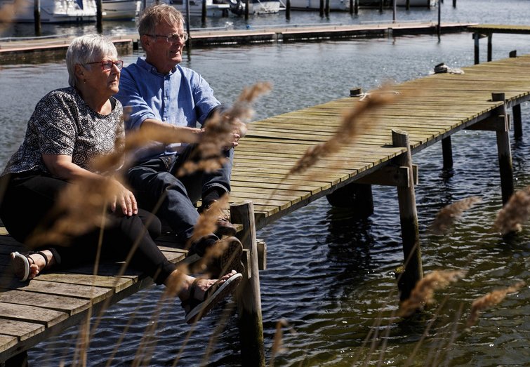 Eva og Thorsteinn sidder på badebro ned til Skælskør Fjord foran deres hus