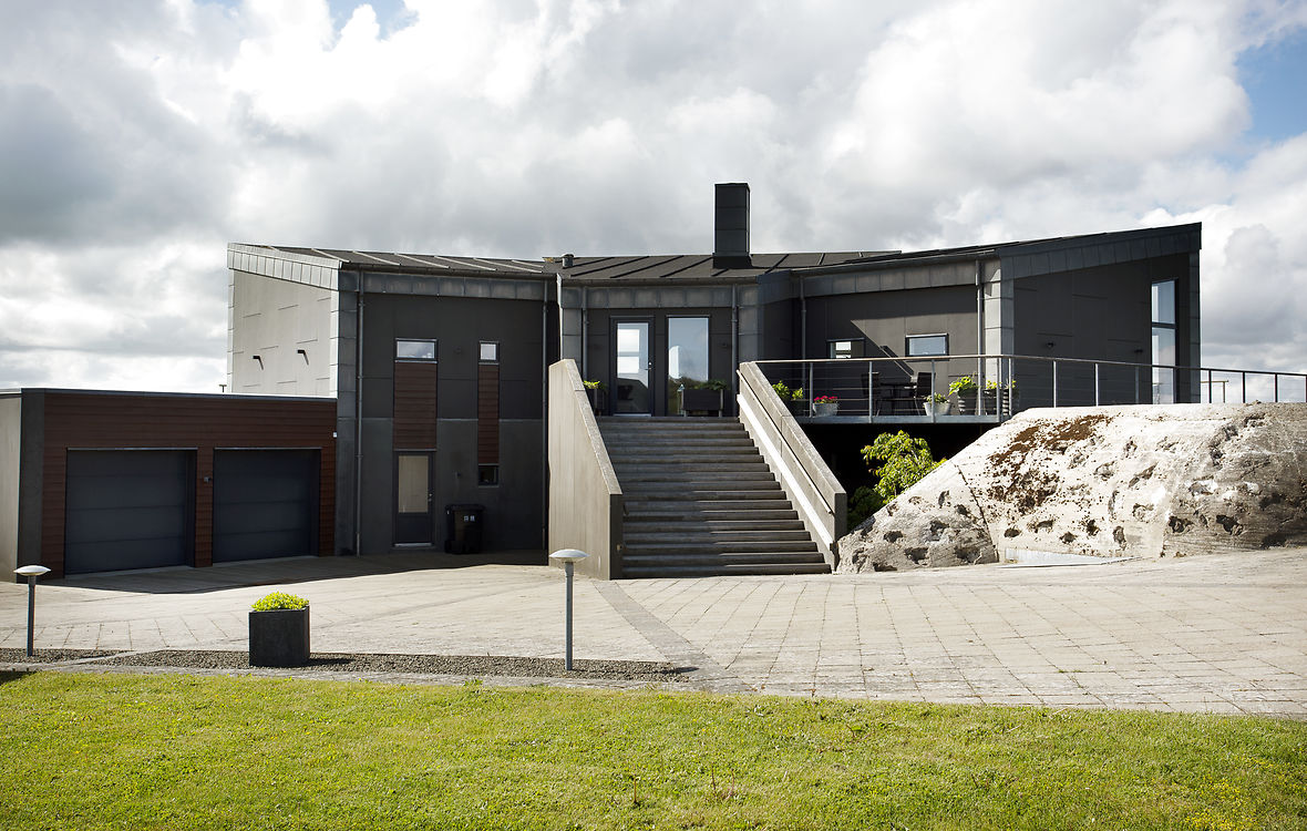 Bagsiden af huset med bunker og stor trappe til 1. sal Billedtekst: Husets forside ligger mod syd og vendt mod udsigten. Derfor kører man også til husets bagside fra villavejen, hvor bunkeren byder velkommen som det første.