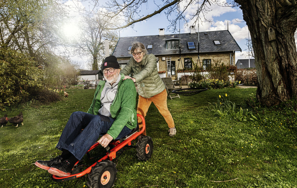 Lise Palm skubber sin mand, Peter Aalbæk Jensen, på en mooncar, med deres hus i baggrunden.