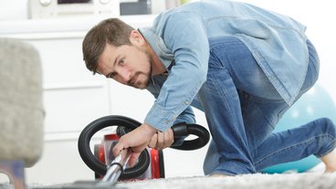 mand støvsuger gulvtæppe foran sofa